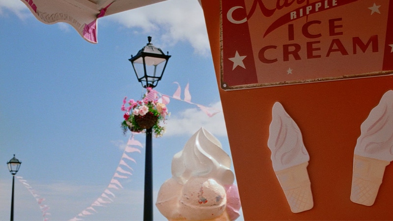 Una persona vestida de rosa toma un helado y luego camina por un muelle con accesorios coloridos de playa.