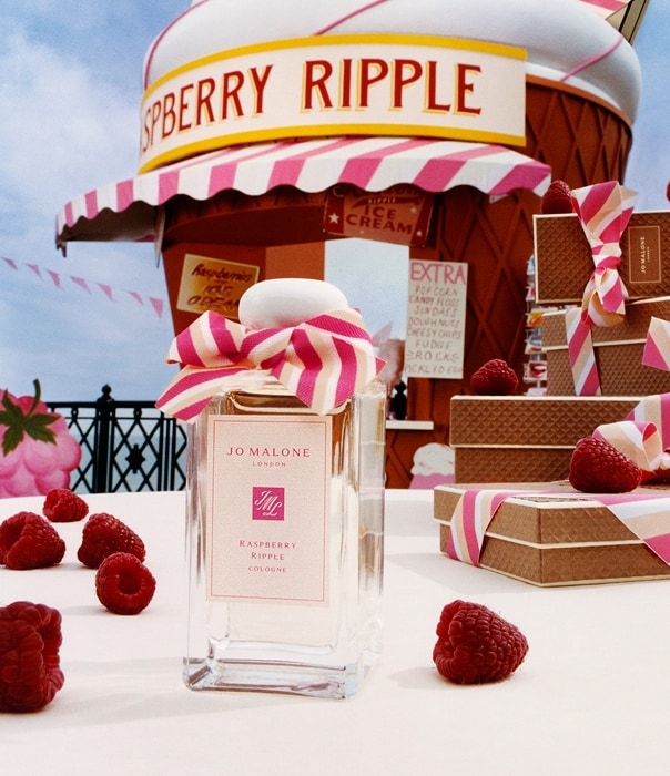 Una fragancia de Jo Malone London con lazo rosa rodeada de frambuesas y una caseta gigante de cono, junto a cajas de regalo.