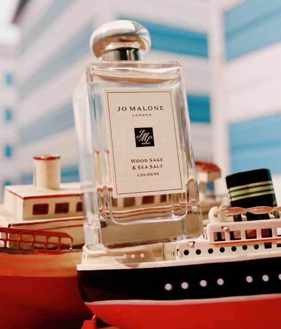 Una fragancia de Jo Malone London sobre pequeños botes de modelo con un fondo de casetas de playa azules y blancas.